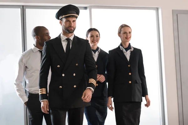 Piloto bonito andando pelo aeroporto com sua equipe — Fotografia de Stock