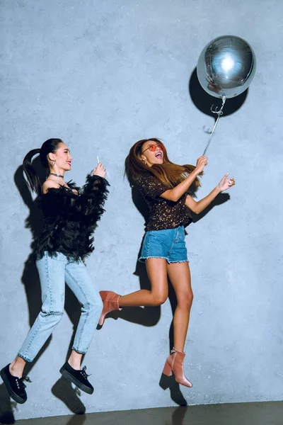 Beautiful stylish multiethnic girls having fun with balloon and smartphone at party — Stock Photo