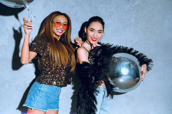 Beautiful stylish multiethnic women holding balloons and smiling at camera — Stock Photo