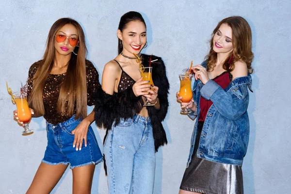 Schöne, stylische multiethnische Frauen, die Gläser mit Cocktails halten und in die Kamera lächeln — Stockfoto