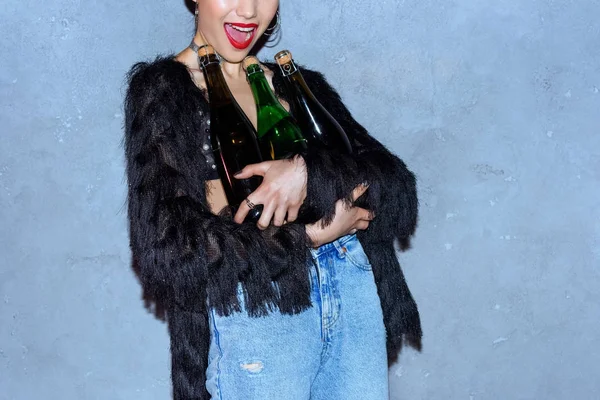 Обрізаний знімок стильної молодої жінки, що тримає пляшки з алкогольними напоями на сірому — стокове фото