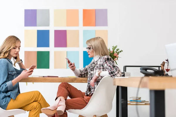 Modische Zeitschriftenredakteure arbeiten mit Smartphones am Arbeitsplatz mit Farbpalette an der Wand — Stockfoto