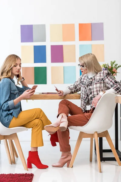 Éditeurs de magazines travaillant avec des smartphones sur le lieu de travail avec palette de couleurs sur le mur — Photo de stock