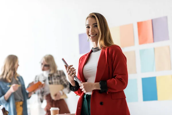 Asian magazine editors with documents in modern office with coworkers behind — Stock Photo