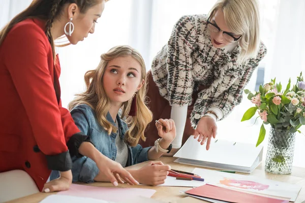 Modische multiethnische Magazinredakteure, die mit Skizzen im modernen Büro arbeiten — Stockfoto