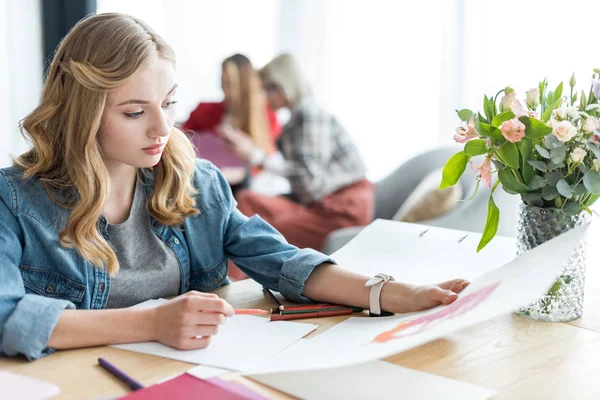 Beautiful magazine editor drawing sketches in modern office, coworkers sitting behind — Stock Photo