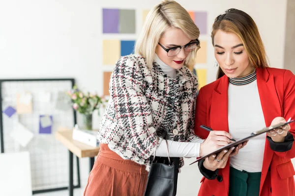 Éditeurs de magazines multiethniques travaillant avec des documents sur presse-papiers dans le bureau moderne — Photo de stock