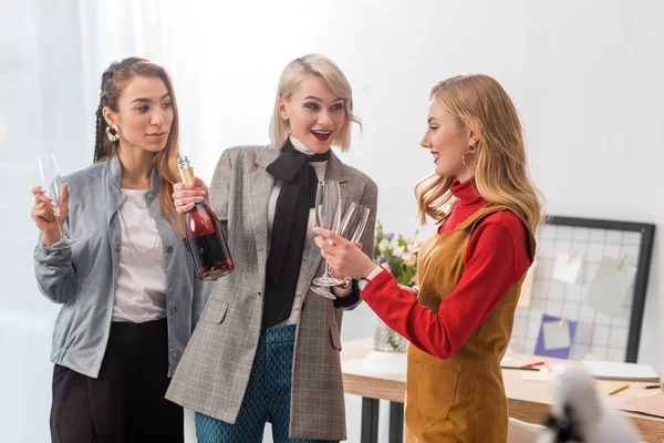 Excited magazine editors celebrating with champagne in modern office — Stock Photo