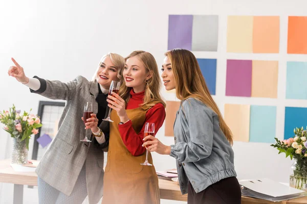 Multiethnic magazine editors celebrating with champagne and pointing somewhere in modern office — Stock Photo
