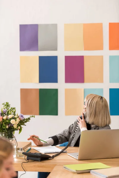 Éditeur de magazine parlant au téléphone et regardant la palette de couleurs sur le mur — Photo de stock