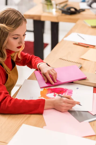 Attraktiver Redakteur für Modezeitschriften, der im modernen Büro mit Skizzen und Dokumenten arbeitet — Stockfoto