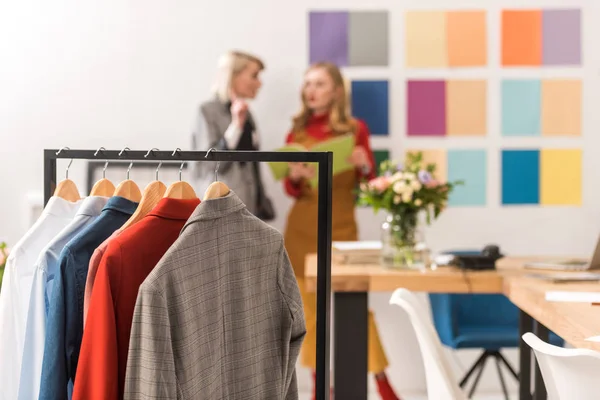 Costureiras elegantes que trabalham no escritório moderno com roupas em primeiro plano — Fotografia de Stock