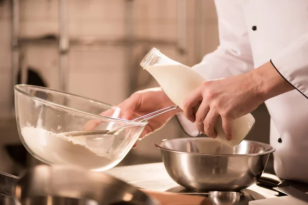 Partial view of confectioner adding milk into dough in restaurant kitchen — Stock Photo