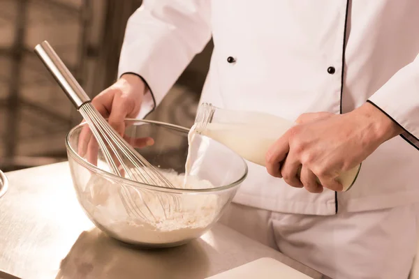 Partial view of confectioner adding milk into dough in restaurant kitchen — Stock Photo