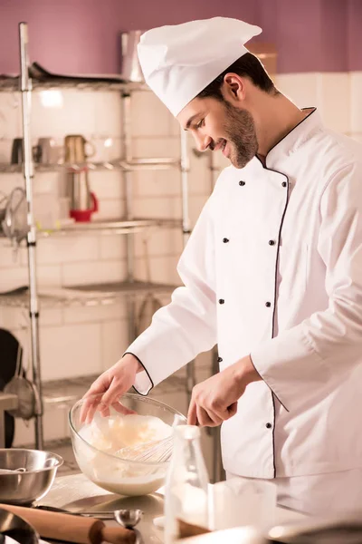 Pastelero alegre en sombrero de chef haciendo masa en la cocina del restaurante — Stock Photo