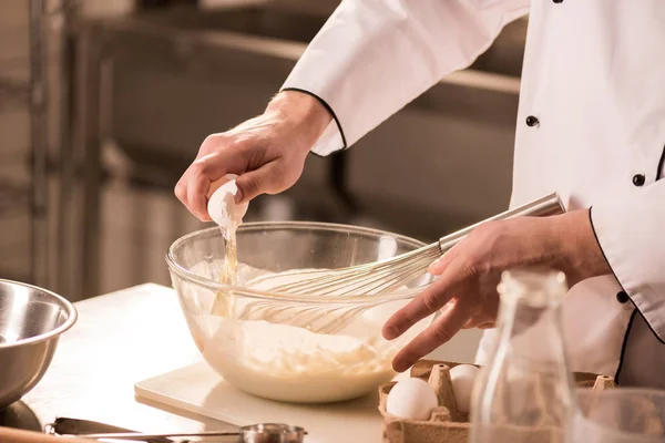 Partial view of confectioner adding raw egg into dough in restaurant kitchen — Stock Photo