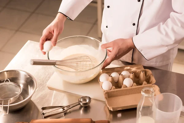 Partial view of confectioner adding raw egg into dough in restaurant kitchen — Stock Photo