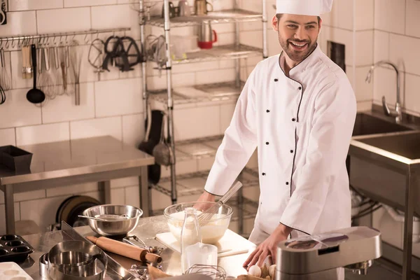 Pastelero alegre de pie en el mostrador en la cocina del restaurante - foto de stock