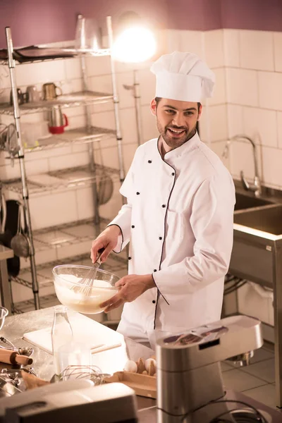 Lächelnder Konditor mit Kochmütze macht Teig in Restaurantküche — Stockfoto