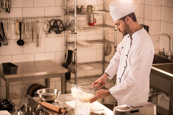 Side view of confectioner in chef hat making tough in restaurant kitchen — стоковое фото