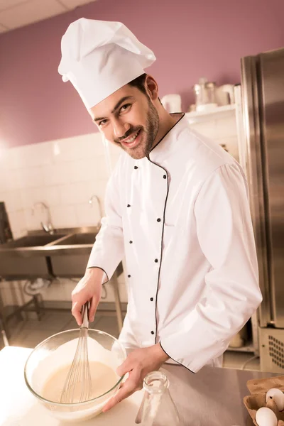 Retrato de confitero sonriente en sombrero de chef haciendo masa en la cocina del restaurante - foto de stock