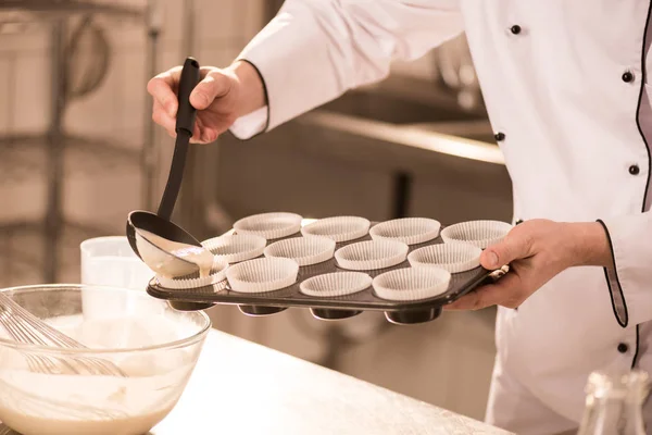 Partial view of confectioner pouring dough into baking forms — Stock Photo
