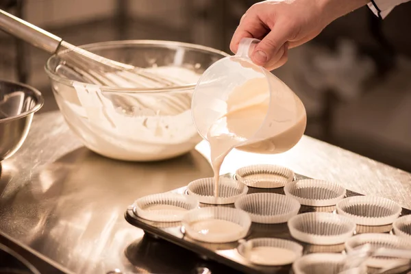 Tiro cortado de massa de confeiteiro derramando em formas de cozimento — Fotografia de Stock