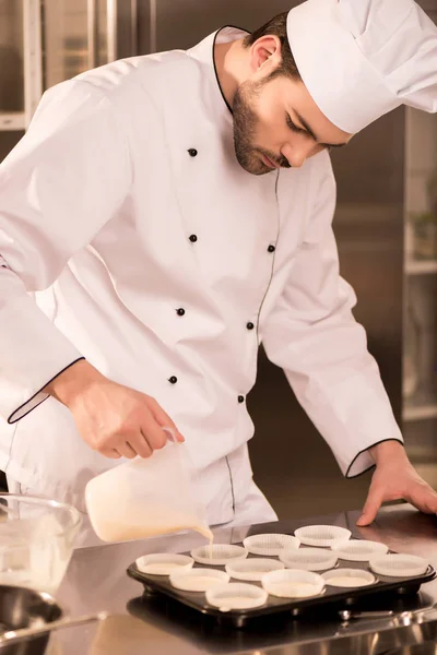 Portrait of confectioner pouring dough into baking forms in restaurant kitchen — Stock Photo