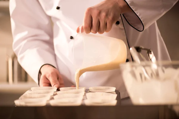 Tiro cortado de massa de confeiteiro derramando em formas de cozimento — Fotografia de Stock