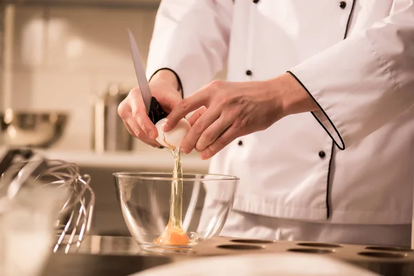 Cropped shot of confectioner breaking egg into bowl while making dough — Stock Photo