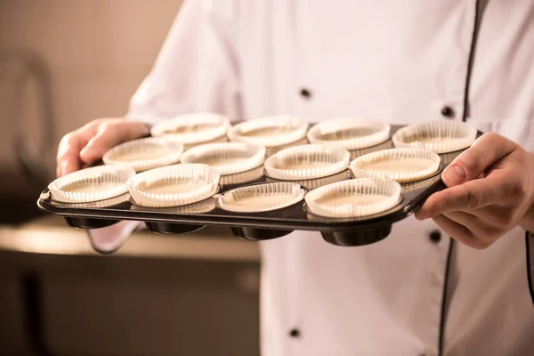 Vista parziale del pasticciere con forme di cottura al forno piene di pasta cruda in mano — Foto stock