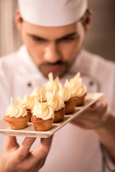 Selective focus of confectioner looking at cupcakes on plate in hands — Stock Photo