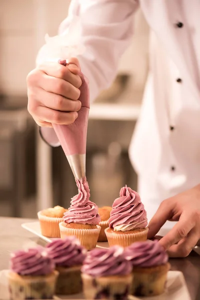 Tiro cortado de confeiteiro colocando creme em cupcakes — Fotografia de Stock