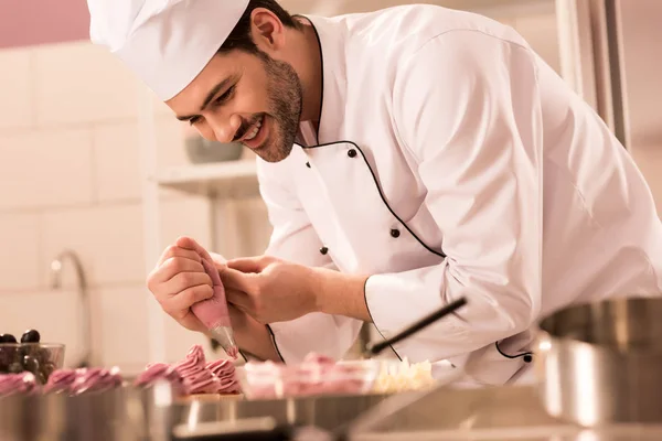 Confectioner decorating cupcakes with cream in restaurant kitchen — Stock Photo