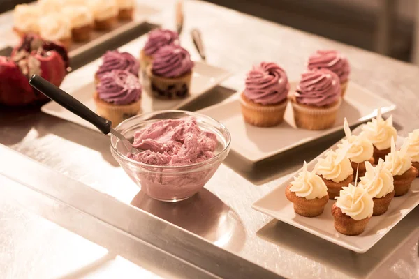 Close up view of cream and sweet cupcakes on plates on counter in restaurant kitchen — Stock Photo