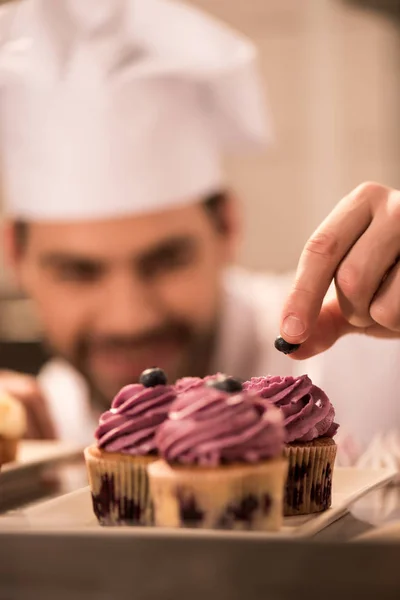 Selective focus of confectioner decorating cupcakes with berries in restaurant kitchen — Stock Photo