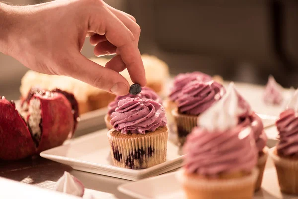 Abgeschnittene Aufnahme eines Konditors, der süße Cupcake mit Beeren dekoriert — Stockfoto