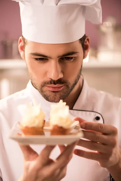 Ritratto di pasticciere focalizzato che guarda cupcake su piatto in mani — Foto stock