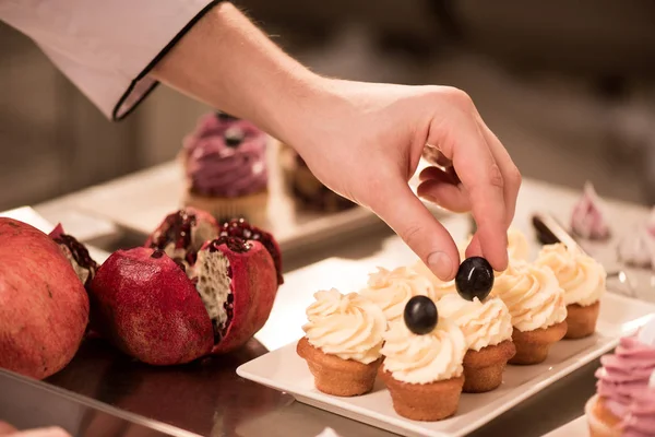 Cropped shot of confectioner decorating sweet cupcakes — Stock Photo