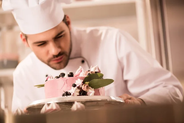 Selective focus of confectioner looking at cake in hands in restaurant kitchen — Stock Photo