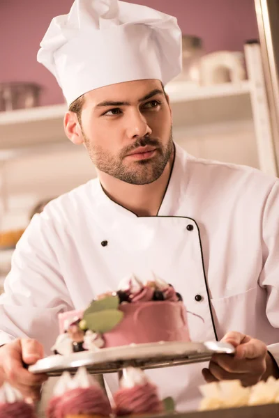 Portrait of confectioner with cake in hands looking away in restaurant kitchen — Stock Photo