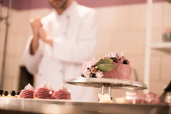 Foco seletivo de bolo, cupcakes e confeiteiro na cozinha do restaurante — Fotografia de Stock