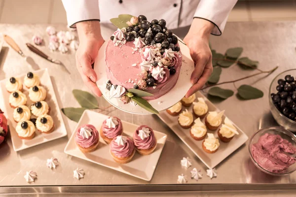 Vista parziale del pasticciere che tiene la torta in mano nella cucina del ristorante — Foto stock