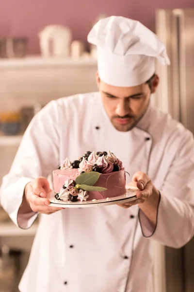 Portrait of confectioner looking at cake in hands in restaurant kitchen — Stock Photo