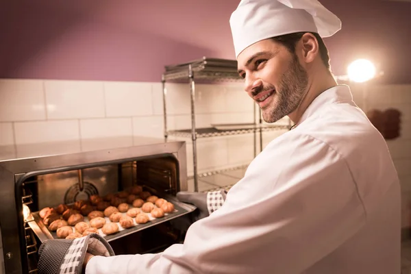 Smiling confectioner holding eclairs on baking pan in hands — Stock Photo