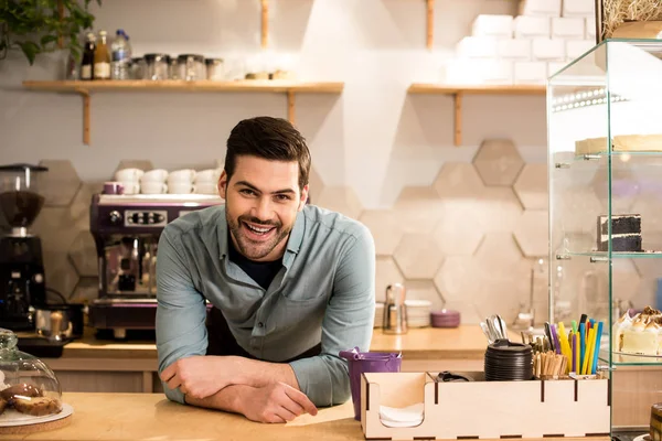 Retrato de barista alegre apoyado en el mostrador en la cafetería - foto de stock