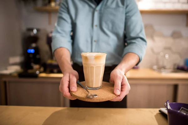 Cropped shot of barista with glass of ice coffee on tray in hands in cafe — Stock Photo