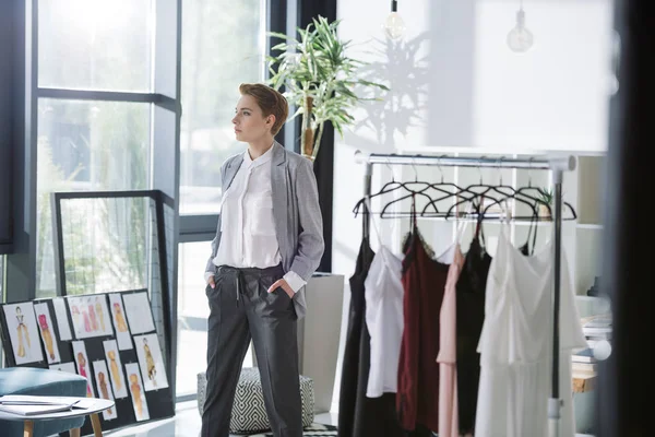 Elegante diseñador de moda en la oficina moderna con muchos vestidos en perchas — Stock Photo