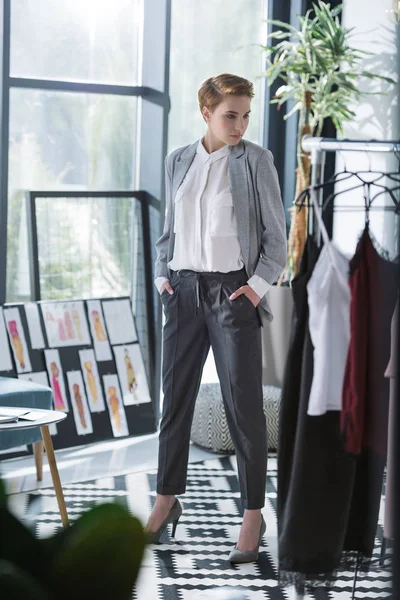 Junge Modedesignerin im modernen Büro mit vielen Kleidern auf Kleiderbügeln — Stockfoto