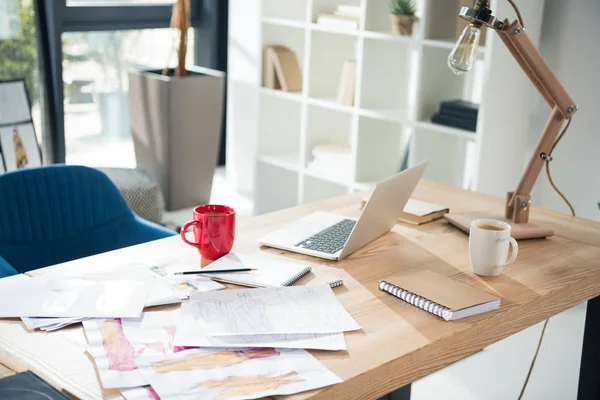 Lieu de travail de créateur de mode désordonné avec ordinateur portable et croquis — Photo de stock